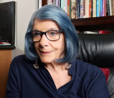 Janet Burroway, sitting, with bookshelves behind.